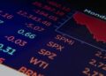 Stock market dashboard featuring rising Nasdaq and Bitcoin graphs with an Iran conflict news ticker.