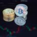 Bitcoin coins stacked with financial charts and graphs in the background, symbolizing investment.