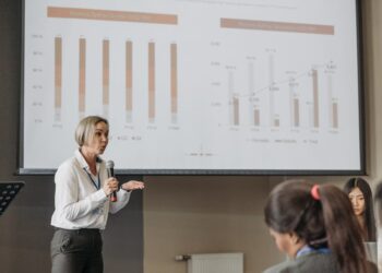 Peter Thiel speaking at a finance conference, with charts and graphs in the background.