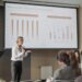 Peter Thiel speaking at a finance conference, with charts and graphs in the background.
